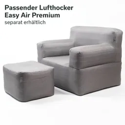 Grauer Sessel mit passenden Hocker, beide aus weichem Material, auf weißem Hintergrund.