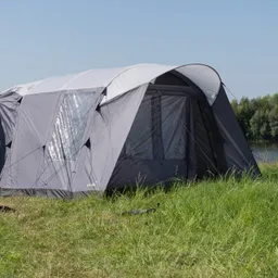Graues Zelt auf einer Wiese mit Sicht auf Wasser und Bäume im Hintergrund unter klarem Himmel.