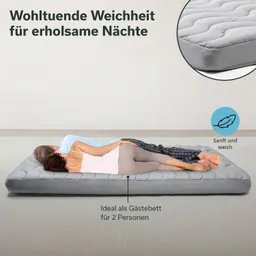 Graue Matratze auf dem Boden mit zwei Personen, die entspannt darauf liegen. Textelemente heben Komfort und Eignung für Gäste hervor.