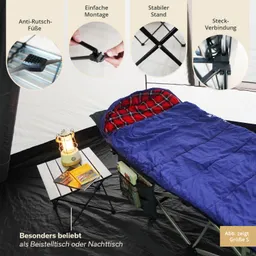 Ein Schlafsack in Blau liegt auf einem Feldbett. Daneben steht ein kleiner Tisch mit einer Lampe und mehreren Büchern.