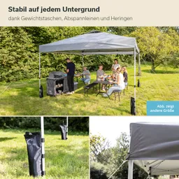 Ein feststehendes Zelt steht auf einem grünen Rasen. Eine Gruppe von Personen sitzt an einem Tisch und isst, während im Hintergrund ein Grill zu sehen ist. Abspannleinen und Gewichtstaschen sind sichtbar.