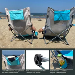 Zwei Klappstühle mit blauer Rückenlehne stehen am Strand, davor das Meer und eine sonnige Himmel.