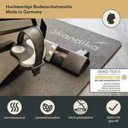 Bodenschutzmatte mit schwarzen und grauen Mustern, teilweise verdeckt von einem Fitnessgerät. Textinformationen und Siegel sind sichtbar.