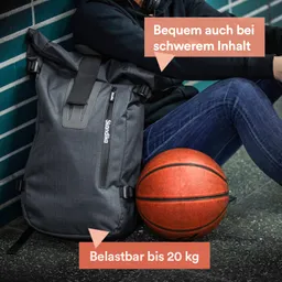 Grauer Rucksack lehnt an einer Wand, daneben ein Basketball. Person sitzt mit Kopfhörern und Jeans.