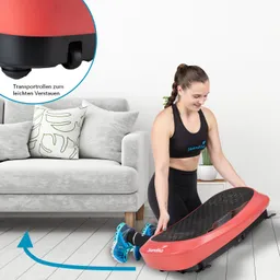 Eine Person kniet auf dem Boden und hebt ein rotes Sportgerät. Im Hintergrund ist ein graues Sofa mit Kissen zu sehen.