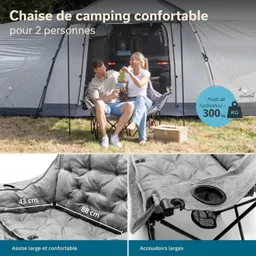 Zwei Personen sitzen auf einer großen Campingliege vor einem Zelt. Die Liege ist grau und bietet Platz für zwei. Im Hintergrund ist ein Zelt und ein Fahrzeug sichtbar.