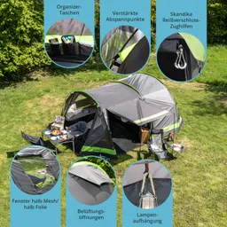 Zelt mit grauen und grünen Akzenten auf einer Wiese, ausgestattet mit Tischen, Stühlen und verschiedenen Taschen.