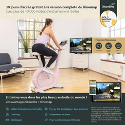 Frau auf einem rosa Fitnessbike in einem hellen Raum, Fernseher und Tablet mit Trainingsvideos sichtbar. Möbel im Hintergrund.