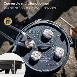 Multifunktionale Pfannenabdeckung auf einem Kochtopf mit zwei Zangen und Kohlenstücken darauf. Maße: 6,5 cm Höhe.