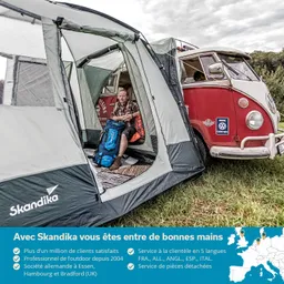 Zelt mit Person im Inneren, die einen Rucksack hält. Im Hintergrund steht ein roter VW-Bus. Grünes Gras und Wolken am Himmel sichtbar.