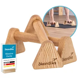Holz-Push-up-Ständer in dreieckiger Form, beschriftet mit "Skandika". Im Hintergrund sind Hände zu sehen, die auf dem Boden aufliegen.