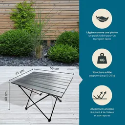 Klappbarer Tisch aus Aluminium auf einem Holzuntergrund, umgeben von grünen Sträuchern und Pflanzen.