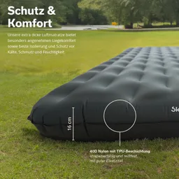 Schwarze Luftmatratze auf grünem Rasen, mit Maßangabe von 16 cm Höhe. Hintergrund: Wald mit Wasserfläche.