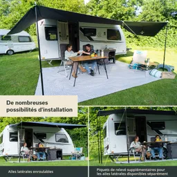 Ein Wohnwagen steht auf einer Wiese mit zwei Personen am Tisch. Der Tisch ist gedeckt, und ein Sonnensegel bietet Schatten.