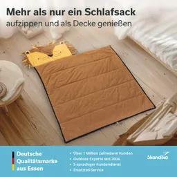 Ein Schlafsack in Form eines Löwenkopfes liegt auf einem Holzboden. Der Schlafsack ist braun und hat einen aufgenähten Löwenkopf.