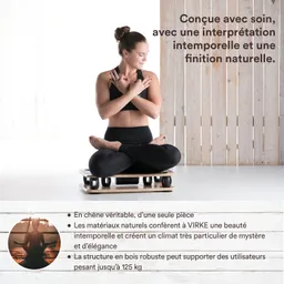 Person in Yogapose mit überkreuzten Beinen auf einem Holzbrett mit Rollen. Heller Hintergrund mit Holzwänden.