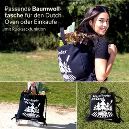 Schwarze Baumwolltasche mit Rucksackfunktion, gefüllt mit Gemüse, getragen von einer Person im Freien. Grafik auf der Tasche zeigt Bäume und Grill.