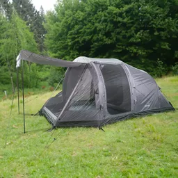 Grau-weißes Zelt auf einer grünen Wiese, umgeben von Bäumen. Ein großer Eingang mit Sichtschutz ist sichtbar.