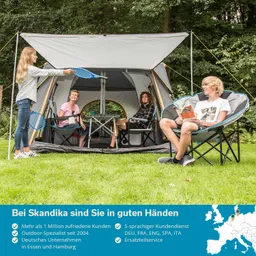 Familie sitzt in einem Pavillon im Freien. Eine Person steht mit einem Schläger, andere lesen oder entspannen.