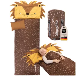 Schlafsack mit Löwen-Motiv und einer Person, die darin liegt und lächelt. Im Hintergrund eine Tragetasche.