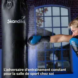 Schwarzer Boxsack mit einem blauen Boxhandschuh, der gerade getroffen wird. Im Hintergrund ein Fenster mit Sicht auf die Außenumgebung.