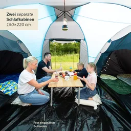 Zelt mit zwei separaten Schlafkabinen. Familie sitzt am Tisch mit Getränken und Snacks. Gras und Bäume im Hintergrund.