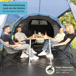 Eine Gruppe von vier Personen sitzt um einen Tisch in einem Zelt. Der Tisch ist mit Lebensmitteln und Getränken gedeckt. Die Zeltinnenwände sind schwarz, und der Boden ist dunkel.