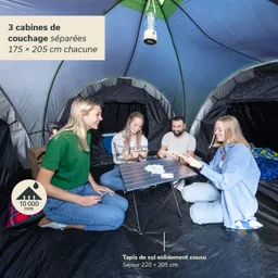 Zelt mit 4 Personen, die um einen kleinen Tisch sitzen und Karten spielen. Zeltinnenseite in Blau und Grün, mit Schlafkabinen.