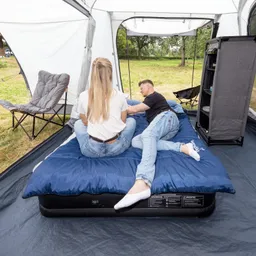 Luftbett in einem Zelt mit zwei Personen, die entspannt nebeneinander sitzen, umgeben von Campingmöbeln und Natur.