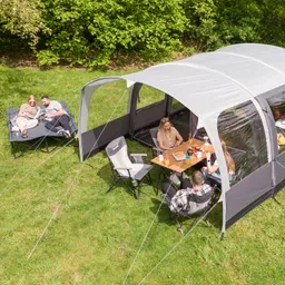 Zelt im Freien mit mehreren Personen in Campingstühlen. Eine Person sitzt an einem Tisch, während andere auf einer Liege entspannen.