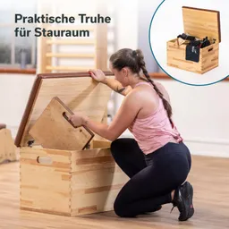 Holzkiste mit Deckel, eine Person kniet daneben und hebt einen Deckel an, im Hintergrund Holzregal.