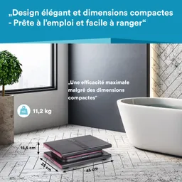Ein kompaktes Gerät liegt auf einem hellen Boden mit Fliesen. Links steht ein Blumentopf mit einer Pflanze. Rechts ist eine weiße Badewanne.
