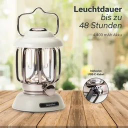 Tischlaterne mit metallischem Gestell, weißen und transparenten Elementen, auf einem Holztisch. Im Hintergrund Pflanzen.