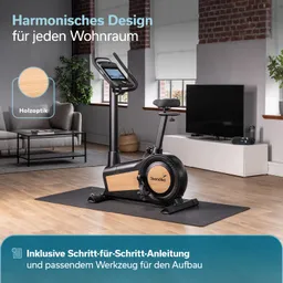 Heimtrainer mit Holzoptik in einem modernen Raum, Wohnzimmermöbel und TV im Hintergrund. Mattenunterlage sichtbar.