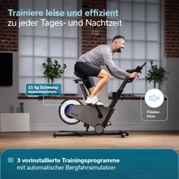 Ein Heimtrainer steht in einem Raum. Eine Person sitzt auf dem Fahrrad und trainiert. Hinter der Person sind große Fenster und eine Pflanze zu sehen.