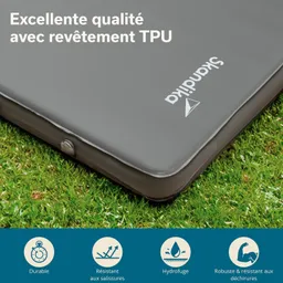 Graue Campingmatte auf grünem Gras mit Logo und Textinformationen zu Eigenschaften wie Haltbarkeit und Wasserresistenz.