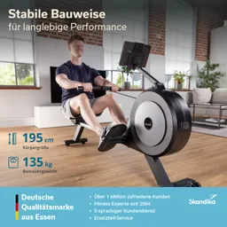 Rudergerät in einem modernen Raum. Eine Person sitzt darauf und rudert. Helle Fenster im Hintergrund, Pflanzen und ein Sofa sichtbar.