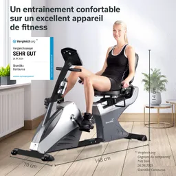 Eine Person sitzt auf einem Fitnessgerät, einem Liegeergometer, in einem Raum mit einem Fenster und einer Pflanze.
