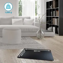 Schwarze Matte mit Maßangaben auf einem Holzfußboden, neben einem grauen Sofa mit weißen Kissen und einem runden Hocker.