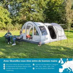 Zelt auf einer Wiese mit zwei Personen an einem Tisch, umgeben von Bäumen.