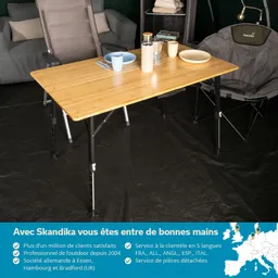 Ein rechteckiger Holztisch steht in einem Innenraum, daneben ein Stuhl. Auf dem Tisch sind Geschirr und eine Thermoskanne platziert.