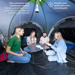 Eine Gruppe von vier Personen sitzt in einem Zelt um einen klappbaren Tisch und spielt Karten. Das Zelt hat eine grüne und graue Innenstruktur.