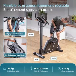 Ergometer in einem Raum mit Holzfußboden. Person justiert das Gerät. Abmessungen und Spezifikationen sind sichtbar.