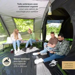 Drei Personen sitzen in einem großen Zelt. Eine Person liest ein Buch, während die anderen miteinander sprechen. Es gibt ein Campbett und einen Laternenhaken im Zelt. Außen ist grünes Gras sichtbar.