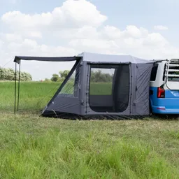 Graues Zelt mit Fenster, verbunden mit einem blauen Fahrzeug, auf einer grünen Wiese unter bewölktem Himmel.