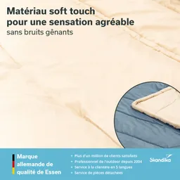 Beige Decke mit weichem Material, in der Ecke ein Ausschnitt einer blauen Fläche. Text in mehreren Sprachen beschreibt die Eigenschaften.