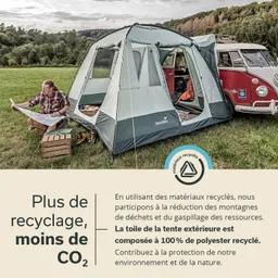 Zelt auf Wiese, Person sitzt mit Karte und Plan, neben rotem VW-Bus, Holzboxen und grüner Landschaft im Hintergrund.
