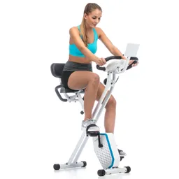 Frau sitzt auf einem Fitness-Bike in blauer Sportoberbekleidung und grauem Shorts, Lenker in Händen haltend.