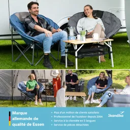 Zwei Personen sitzen in großen, runden Campingstühlen auf einer Wiese. Zwischen ihnen steht ein kleiner Tisch mit Getränken. Im Hintergrund ist ein Wohnmobil sichtbar.