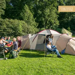 Eine große, helle Campingausrüstung auf Rasen, umgeben von Bäumen. Menschen sitzen an einem Tisch und essen, während andere entspannt auf Stühlen sitzen.